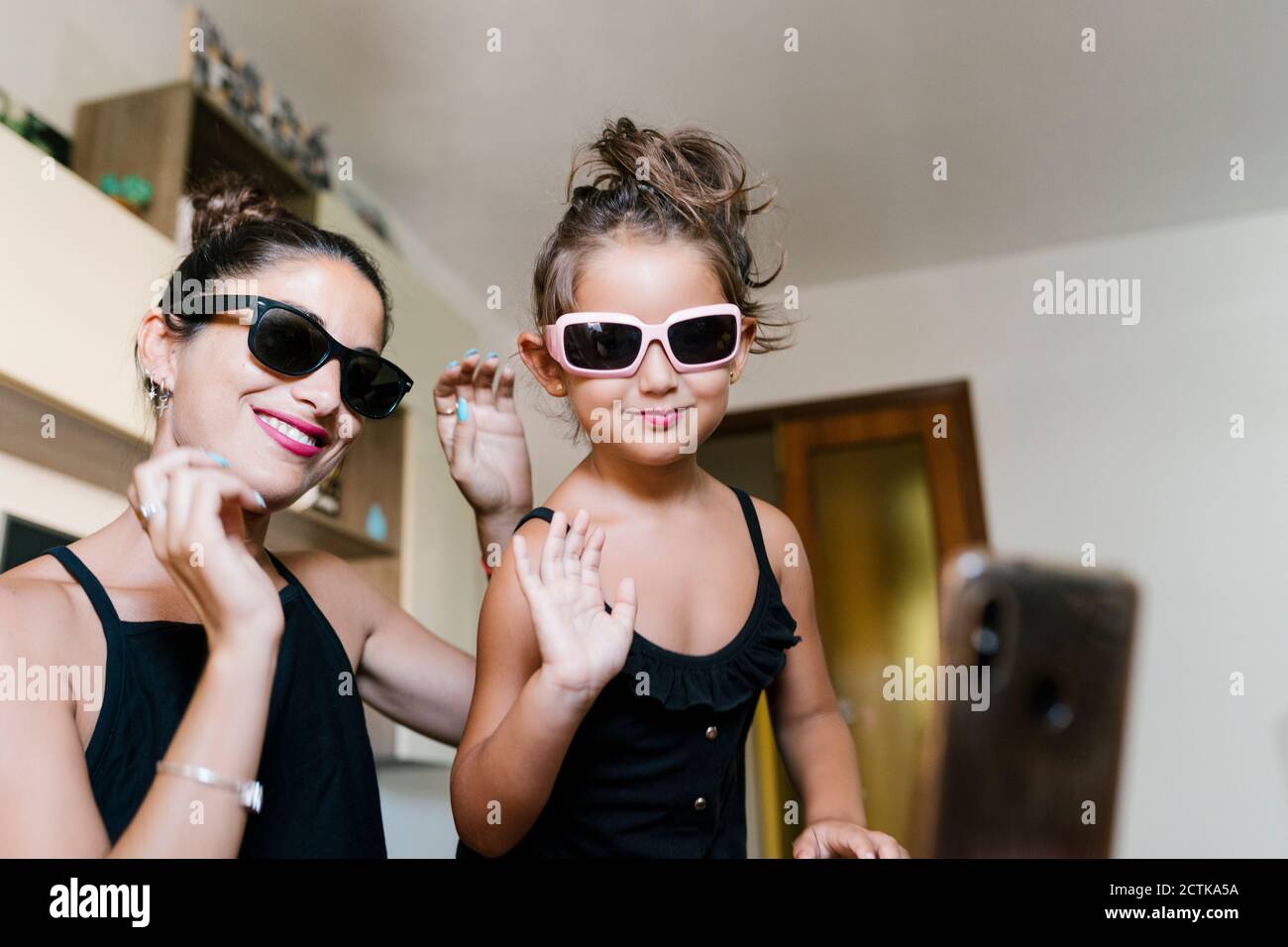 Felice figlia e madre che indossa occhiali da sole durante la registrazione video smartphone a casa Foto Stock