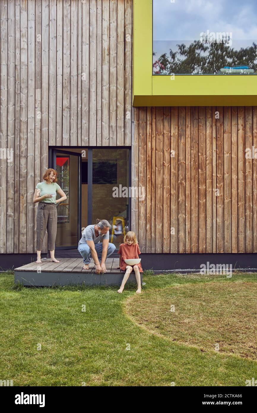 I genitori parlano con la figlia seduta con la ciotola fuori della casa piccola Foto Stock