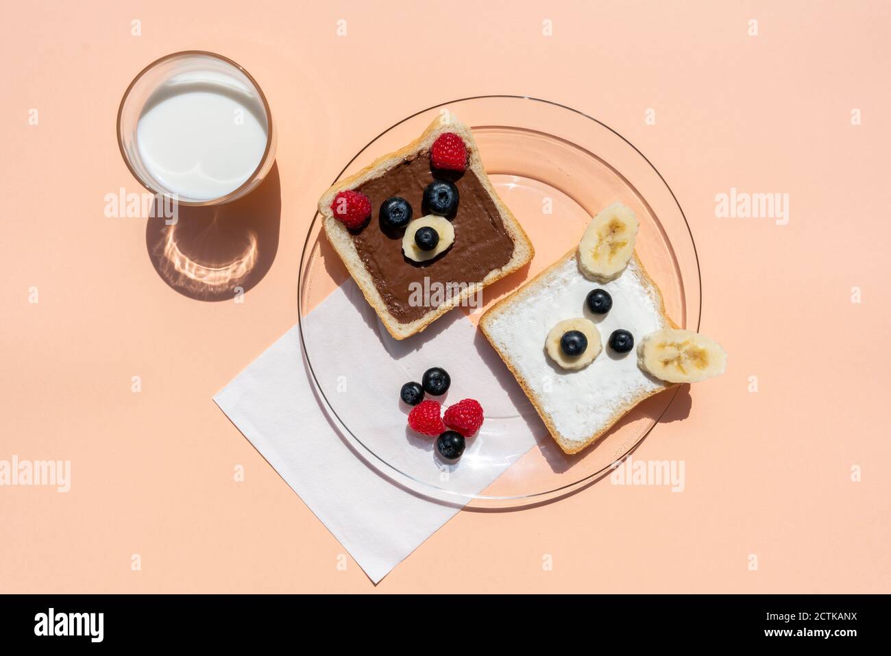 Studio shot di un bicchiere di latte e tostature con orso volti fatti di frutta Foto Stock