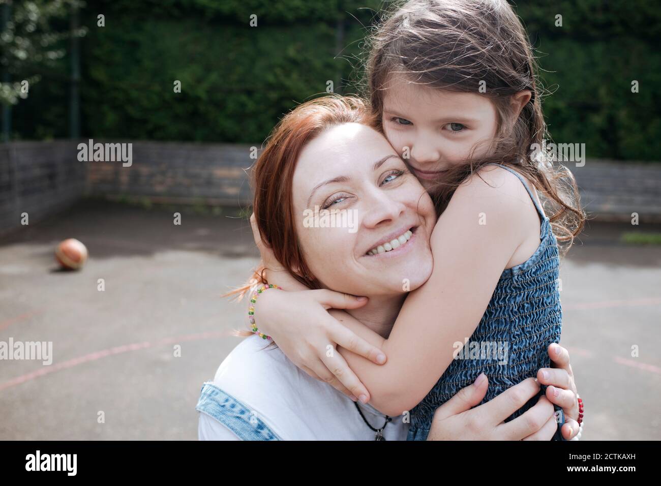 Ragazza abbracciando madre sorridente al campo di pallacanestro nel cortile posteriore Foto Stock
