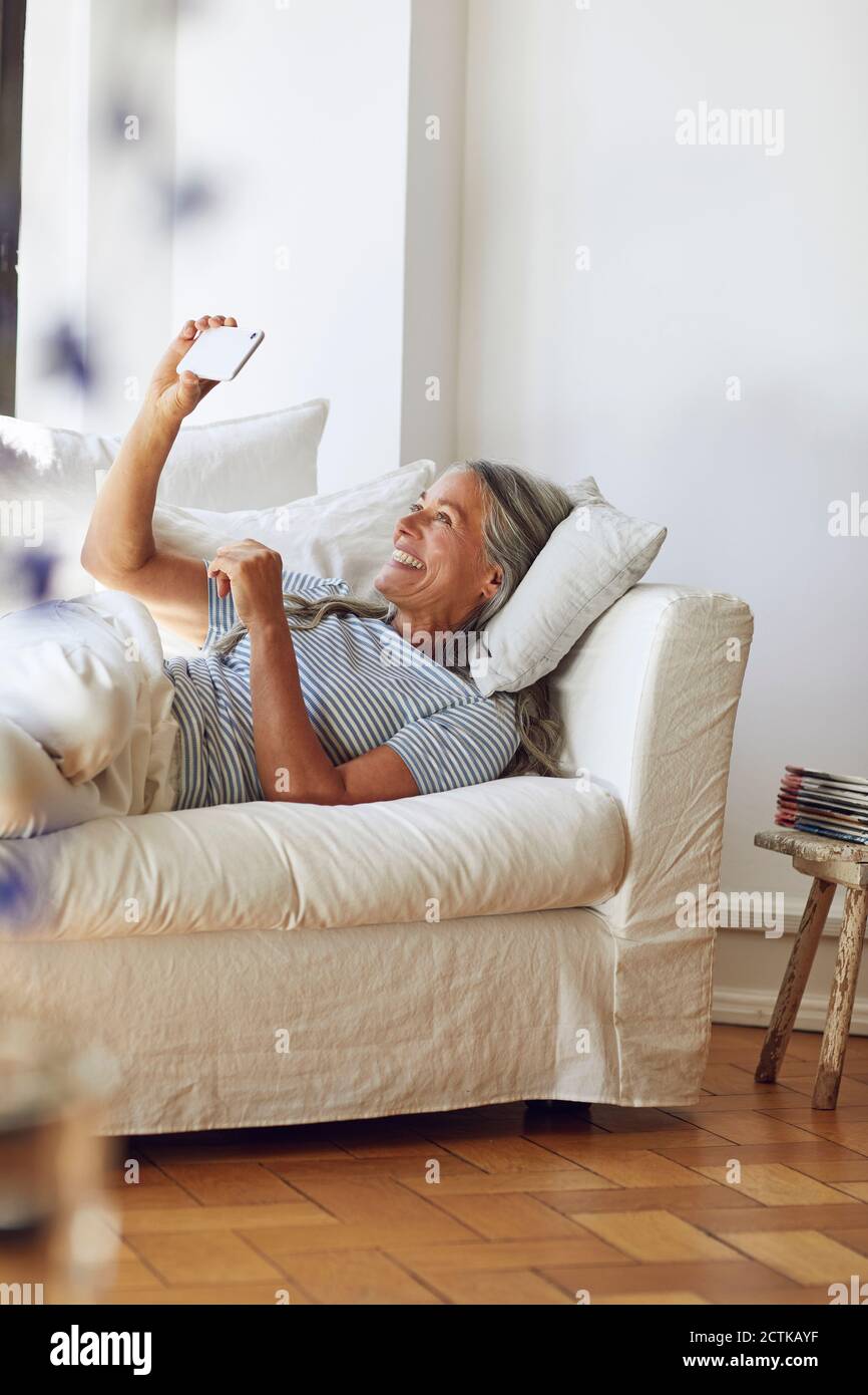 Donna che usa lo smartphone sul divano del soggiorno Foto Stock