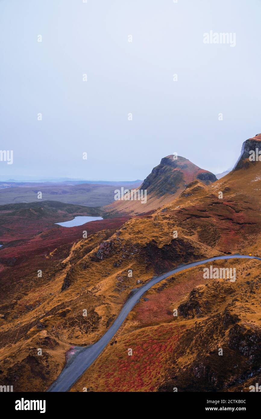 Regno Unito, Scozia, drone vista di vuota autostrada che si estende lungo marrone paesaggio montuoso dell'Isola di Skye con piccolo lago sullo sfondo Foto Stock