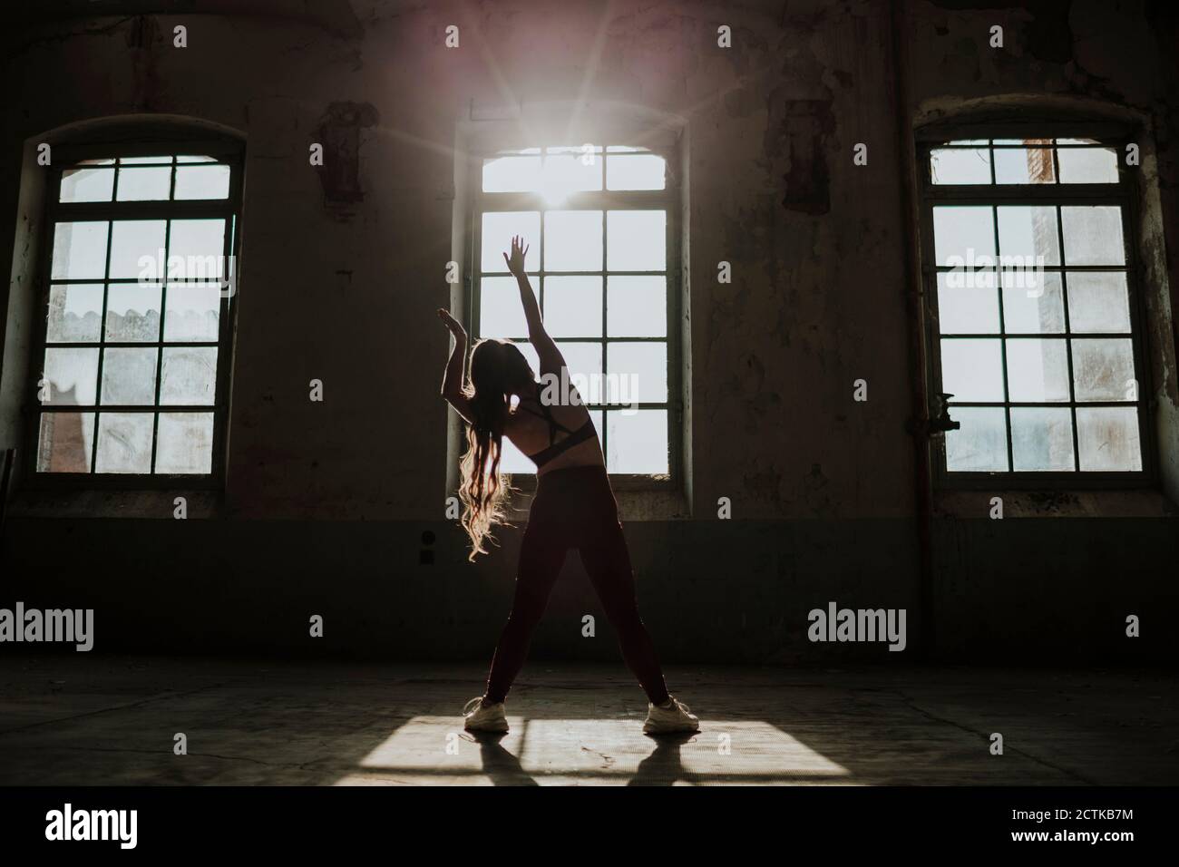 Silhouette di donna che si esercita mentre si sta in piedi alla fabbrica abbandonata Foto Stock