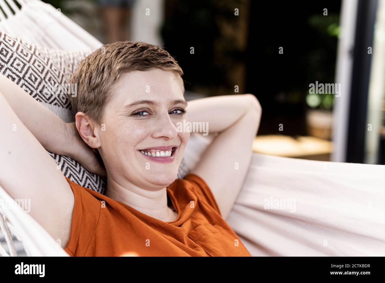 Primo piano di una donna sorridente con le mani dietro la testa che si rilassa amaca in cortile Foto Stock
