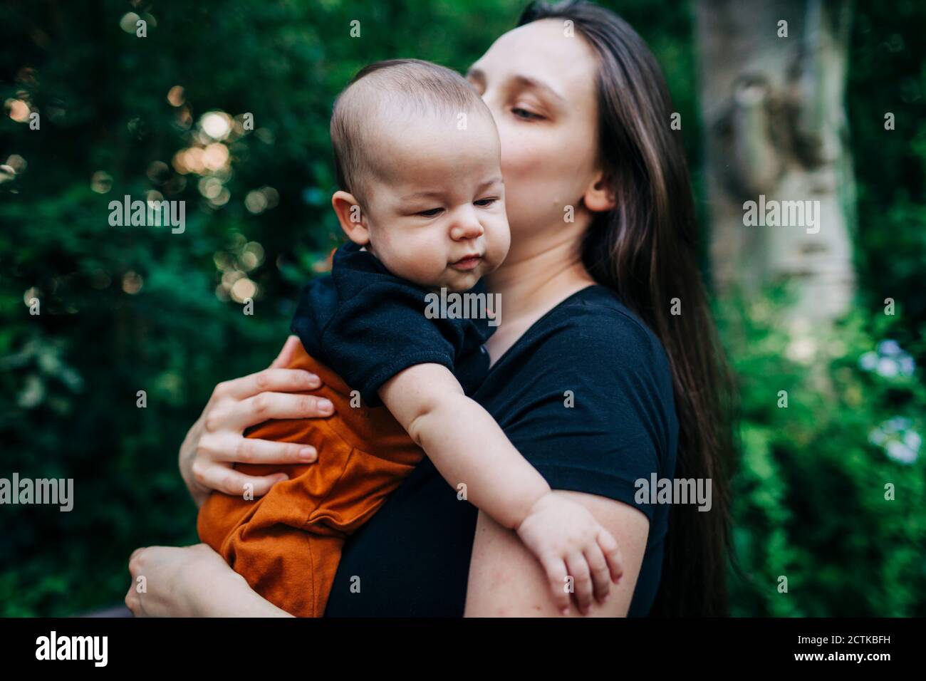 Simpatico bambino tenuto dalla madre al parco durante il fine settimana Foto Stock