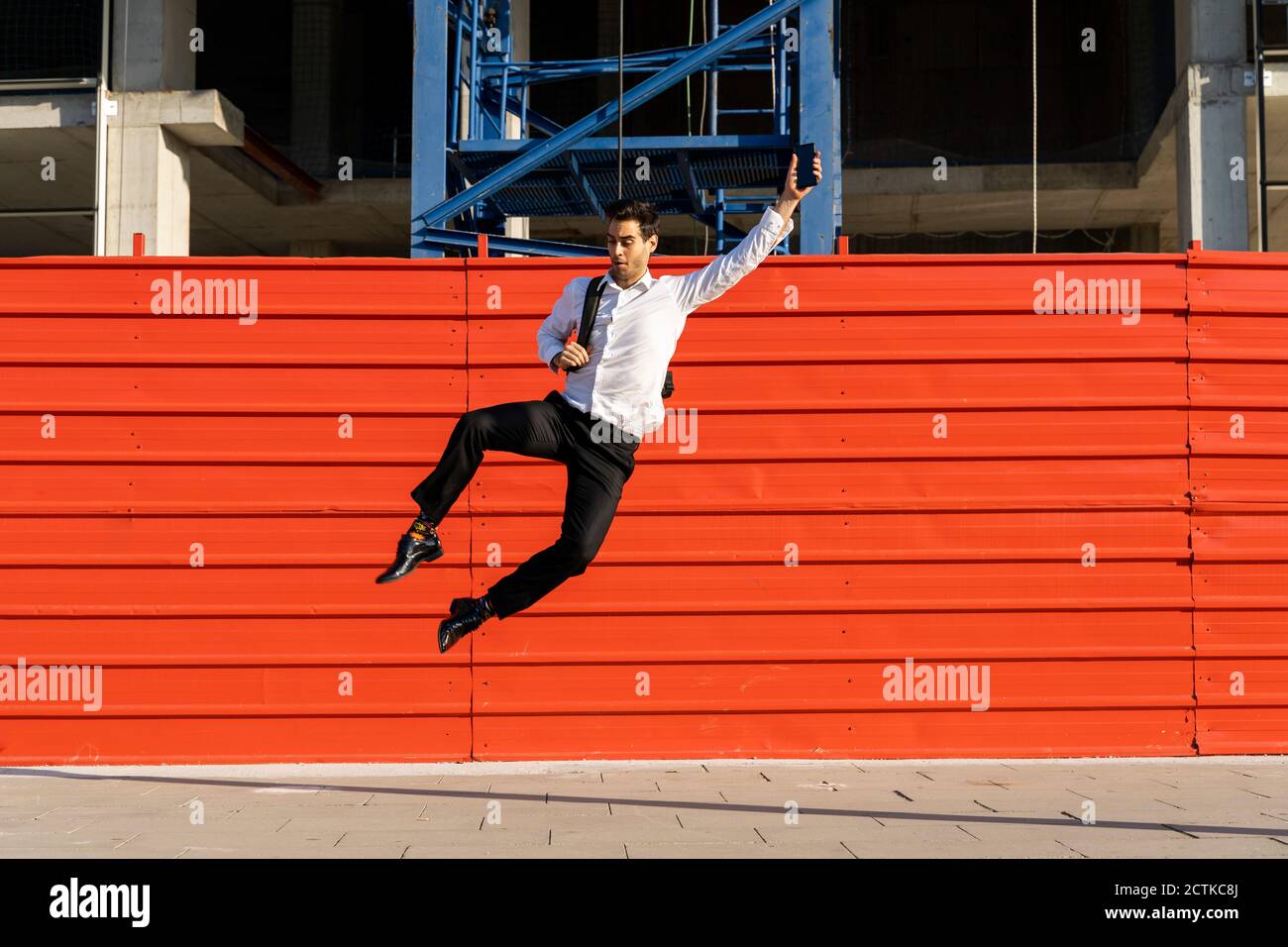 Allegro imprenditore maschile con braccio sollevato saltando sul sentiero contro struttura costruita Foto Stock