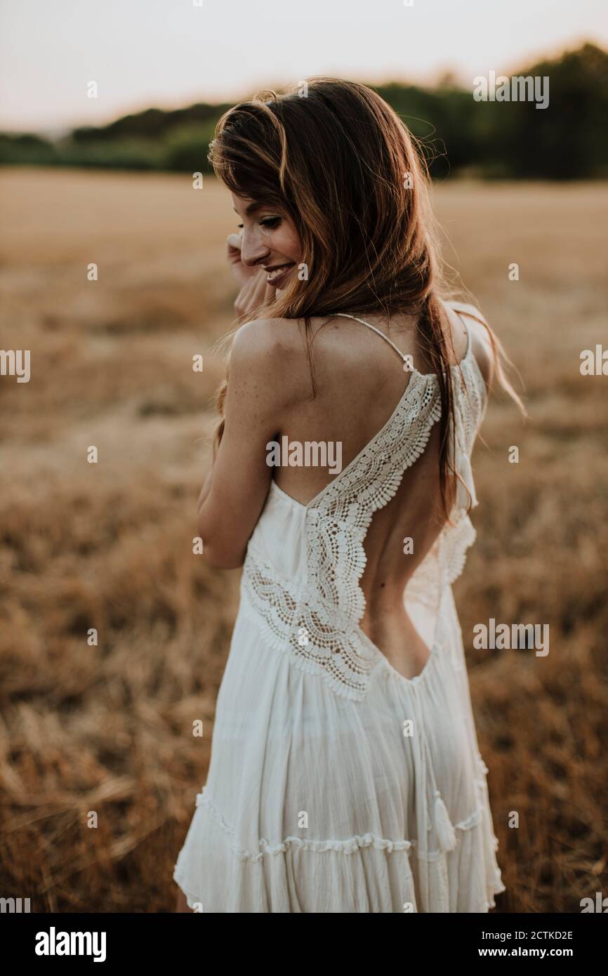 Donna che indossa un abito bianco che si affaccia sulla spalla mentre si sta in piedi campo di grano Foto Stock