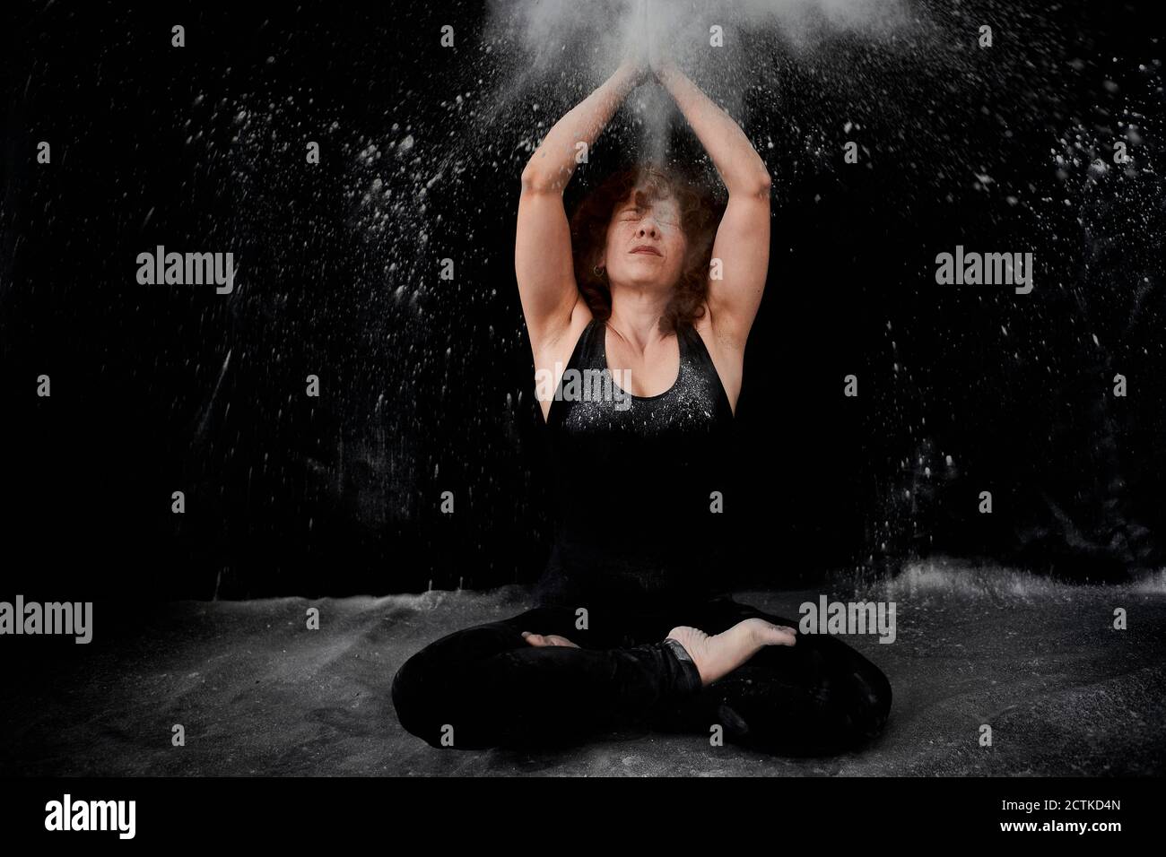 Donna seduta sul pavimento mentre si aggrappava con polvere bianca sopra si è contro sfondo nero Foto Stock