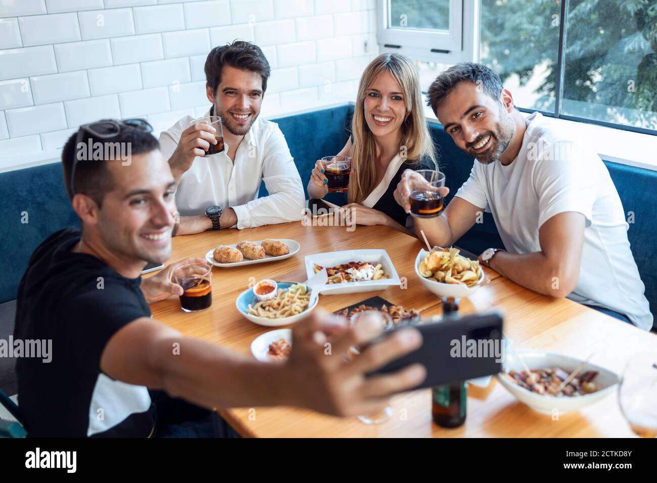 Gruppo di amici che prendono selfie mentre mangiano al ristorante Foto Stock