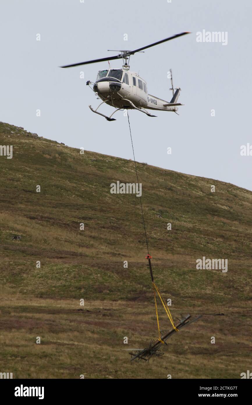 G-UHGB, una Bell 205A-1 gestita dagli specialisti dell'aviazione Heli-Lift Services, durante le operazioni di rimozione di piloni sulle alture del Renfrewshire a Inverclyde, Scozia. I tralicci sono scesi sulla collina e scomposti sul posto, poi rimossi in elicottero in un luogo di discesa dove il metallo viene poi caricato su camion, e infine spostati su strada. Foto Stock