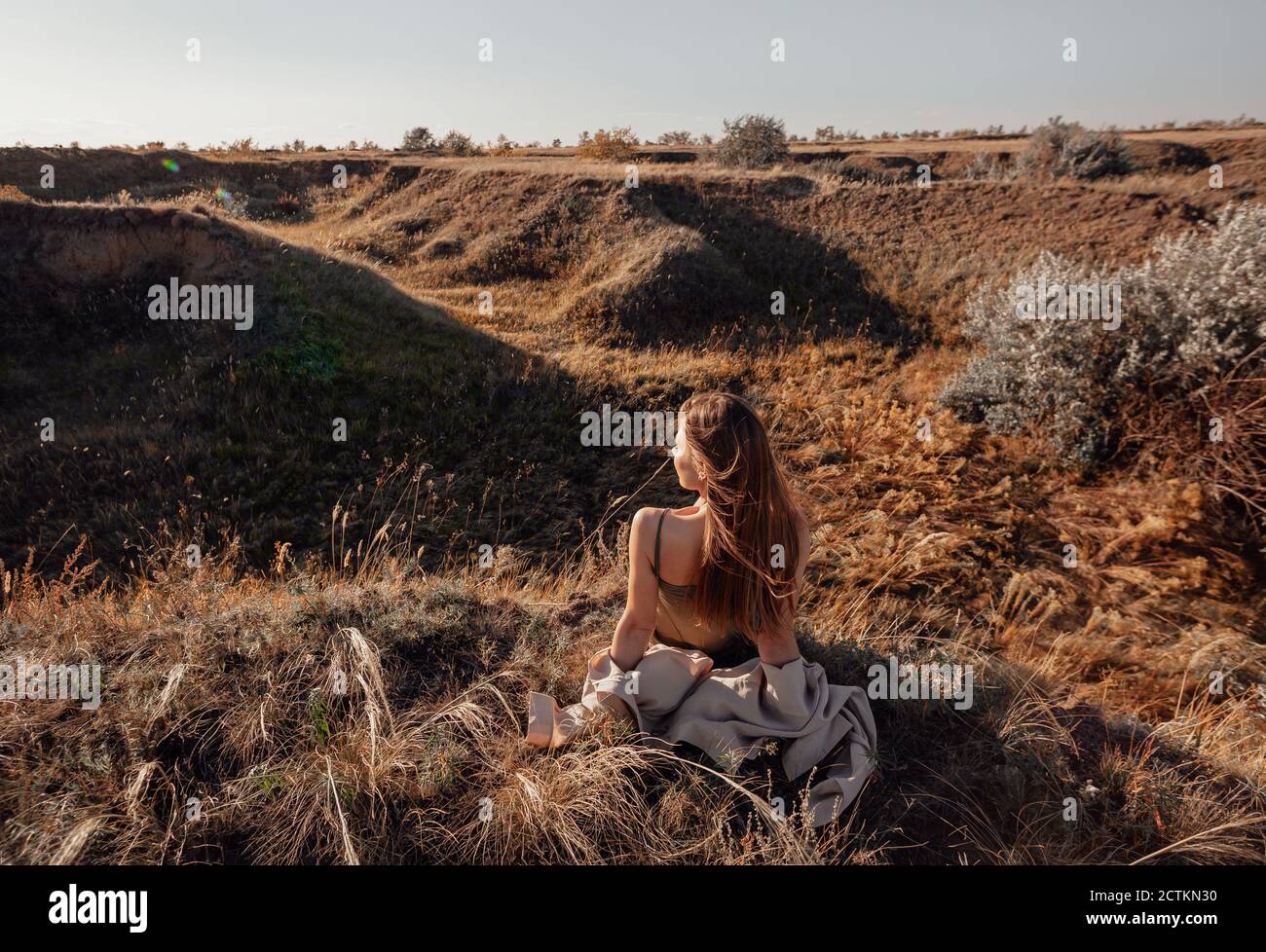 Vista dalla parte posteriore di una ragazza in una camicia seduto su una collina e ammirando la splendida vista e. alba o tramonto Foto Stock