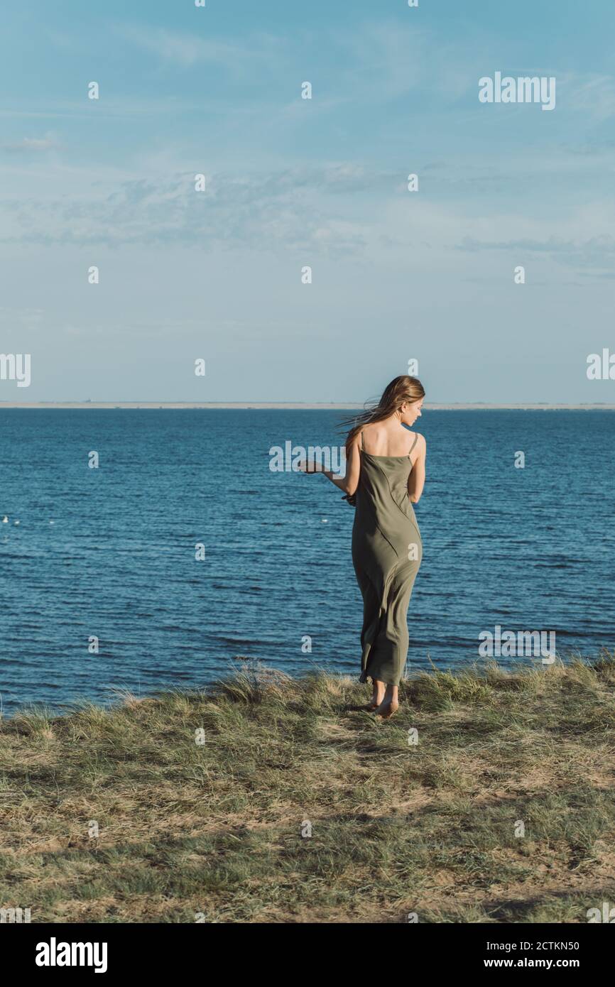 Vista dalla parte posteriore di una ragazza in un abito lungo, in piedi su una scogliera e ammirando la splendida vista del lago. Foto Stock