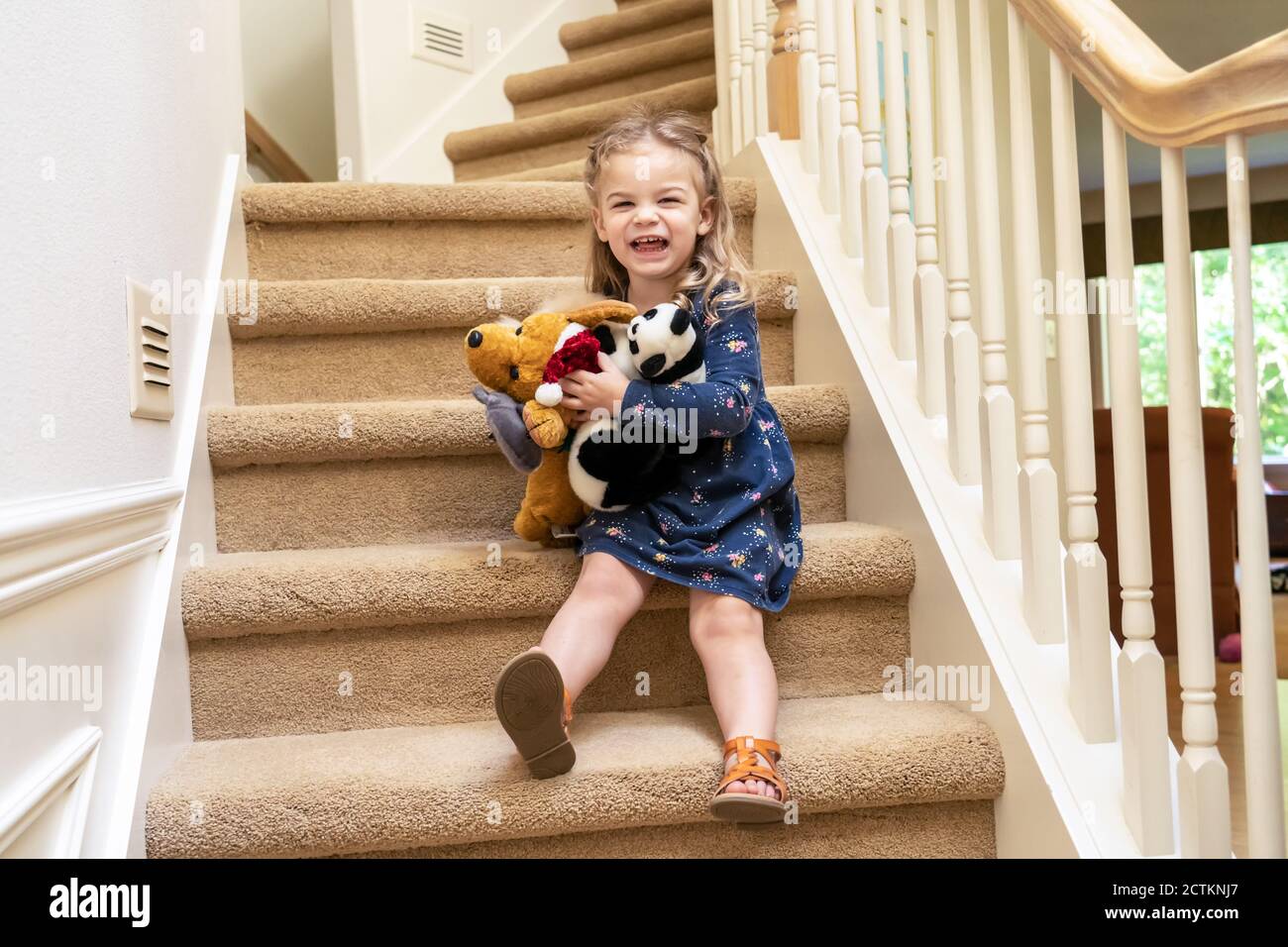 Ragazza di 2.5 anni che gioca con animali imbalsamati sulla scala, scooting cautamente verso il basso (MR) Foto Stock