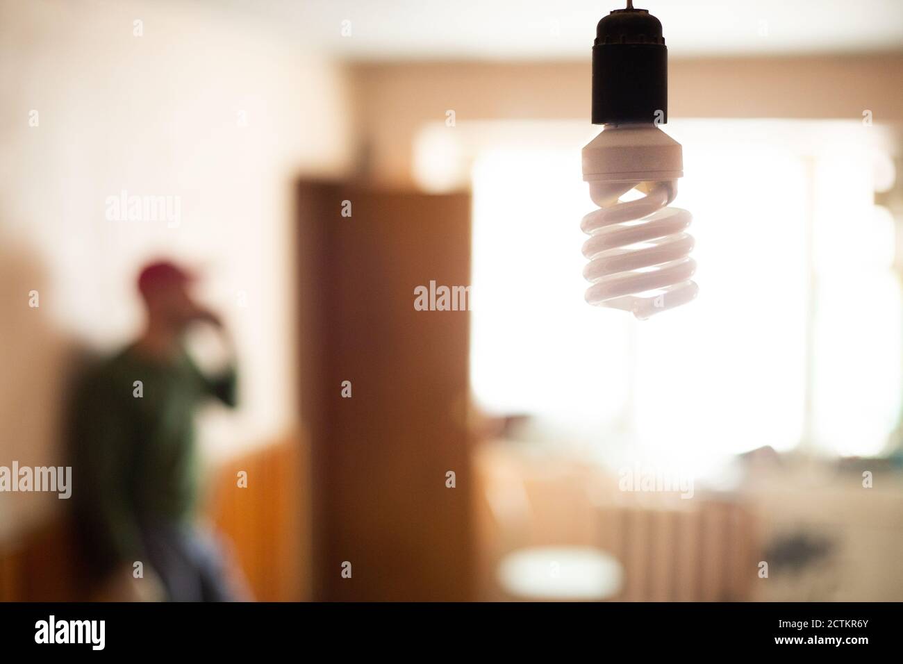 Un uomo, un caposquadra in una cuffia, sta parlando al telefono in una stanza lontana. Sullo sfondo di una lampada a risparmio energetico. Foto Stock