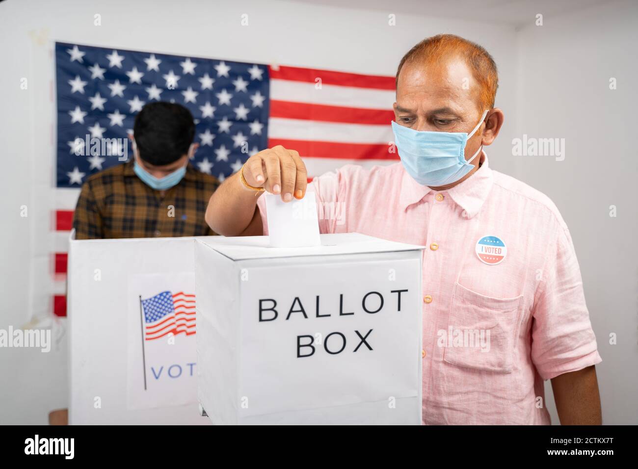 Uomo in maschera medica mettendo carta di voto all'interno della casella di voto - concetto di voto in persona e le persone occupate alla cabina di polling alle elezioni degli Stati Uniti. Foto Stock