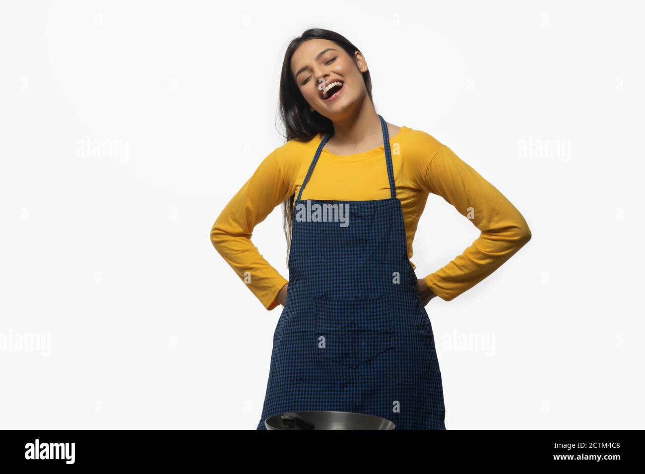 Giovane donna sorridente mentre indossa un grembiule con un wok anteriore Foto Stock