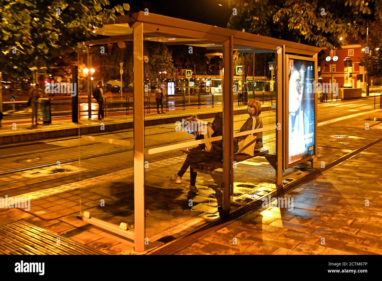 Una giovane donna si siede con una maschera facciale, maschera ad una fermata dell'autobus, fermata del tram, fermata dell'autobus e guarda il suo smartphone, che illumina il suo volto, dopo, il 09/23/2020. | utilizzo in tutto il mondo Foto Stock