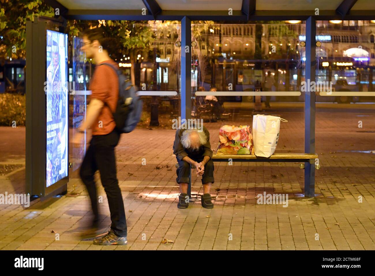 Budapest, Ungarn. 23 Settembre 2020. Un uomo senza casa si siede piegato in avanti ad una fermata dell'autobus - accanto a lui sono due borse di plastica - un passerby, un giovane uomo cammina oltre. Dopo, il 09/23/2020. | utilizzo in tutto il mondo credito: dpa/Alamy Live News Foto Stock