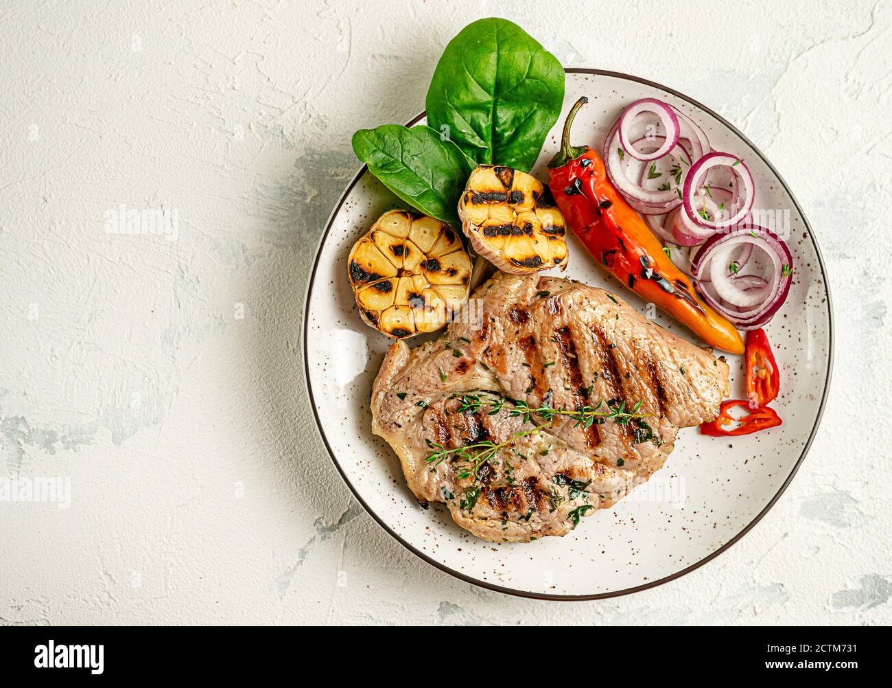 Piatto di bistecca di maiale alla griglia con verdure su fondo di cemento. Concetto di dieta chetogena. Overhead, spazio di copia. Foto Stock