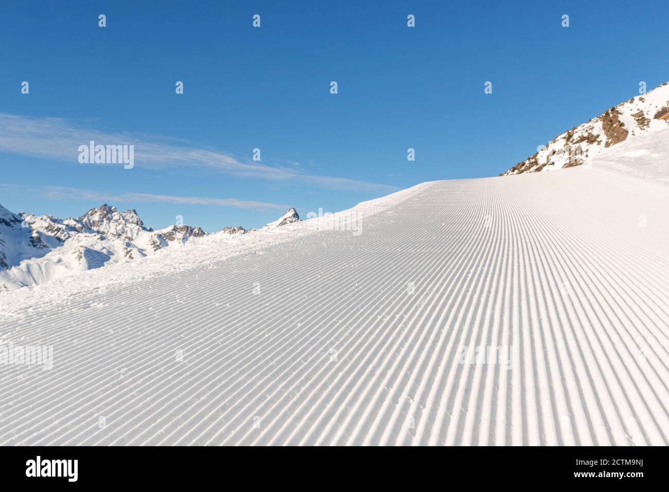 Ranghi retti retti di piste da sci preparate di recente con sole luminoso e cielo blu chiaro sullo sfondo. Montagna innevata Foto Stock