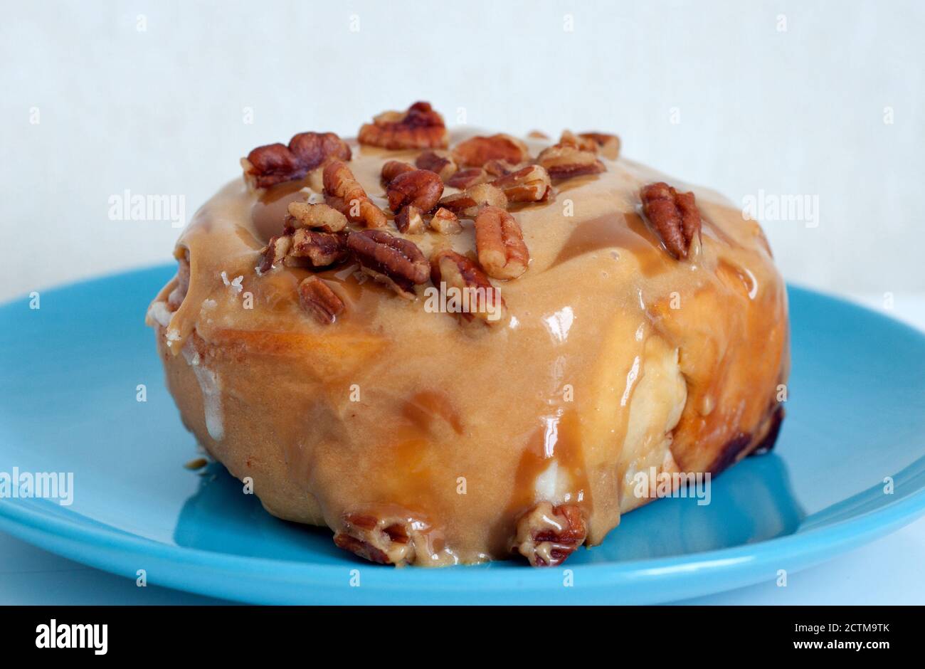 Un dolce panino alla cannella condito con caramello e noci pecan. Dessert su un piatto blu. Foto Stock