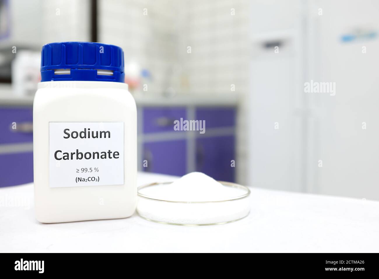 Fuoco selettivo di una bottiglia di composto chimico carbonato di sodio o di carbonato di sodio accanto a una piastra Petri con sostanza in polvere cristallina solida. Laboratorio chimico bianco. Foto Stock
