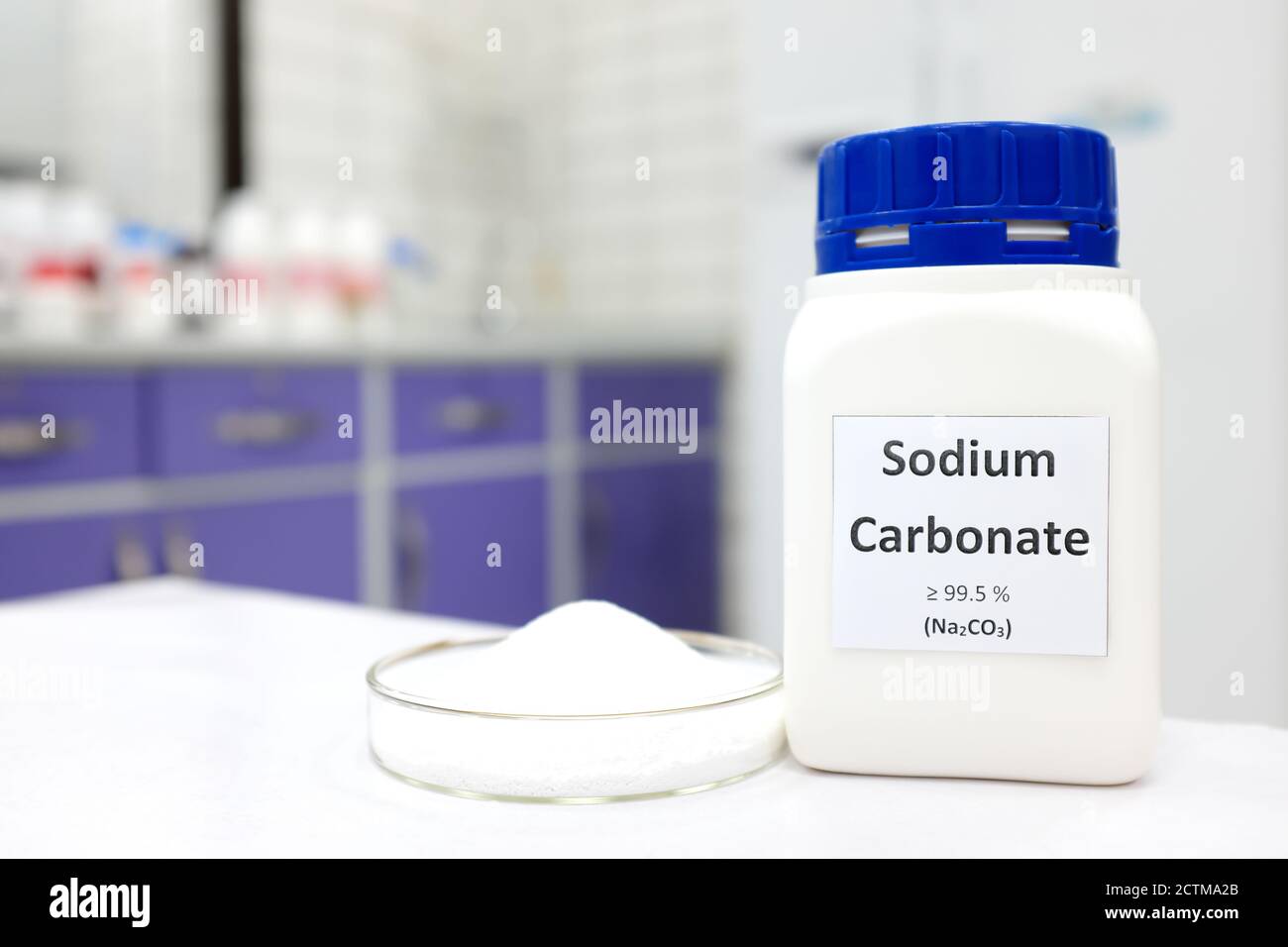 Fuoco selettivo di una bottiglia di composto chimico carbonato di sodio o di carbonato di sodio accanto a una piastra Petri con sostanza in polvere cristallina solida. Laboratorio chimico bianco. Foto Stock