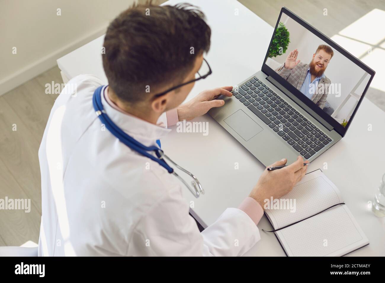 Uomo medico guardando lo schermo del portatile a salutarlo uomo paziente durante la consultazione online Foto Stock