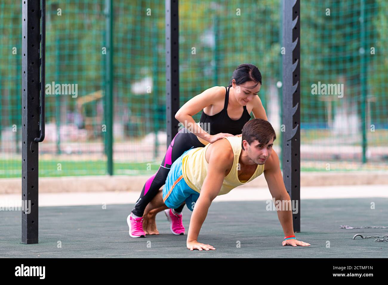 Giovane uomo che lavora fuori facendo i push-up come una giovane donna corre sulla schiena aumentando la resistenza e il carico a un palestra all'aperto in una sala fitness e benessere Foto Stock