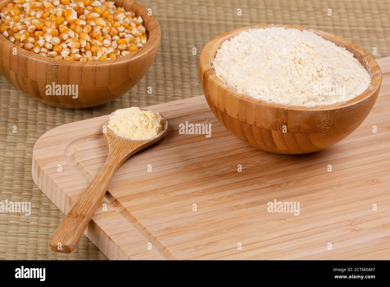 Ciotola di legno di farina di mais o di fiore di mais e cucchiaio di legno pieno di farina di mais su sfondo ligneo Foto Stock