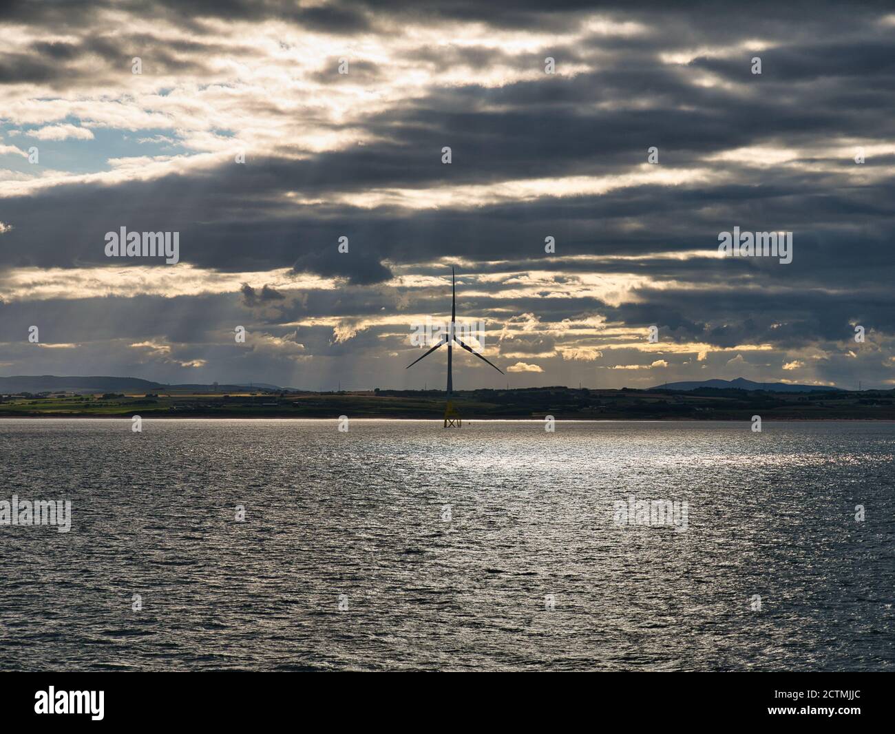 Contro le nuvole scure e il sole luminoso una turbina eolica unica è silhouette al largo delle coste di Aberdeen in Scozia, Regno Unito Foto Stock