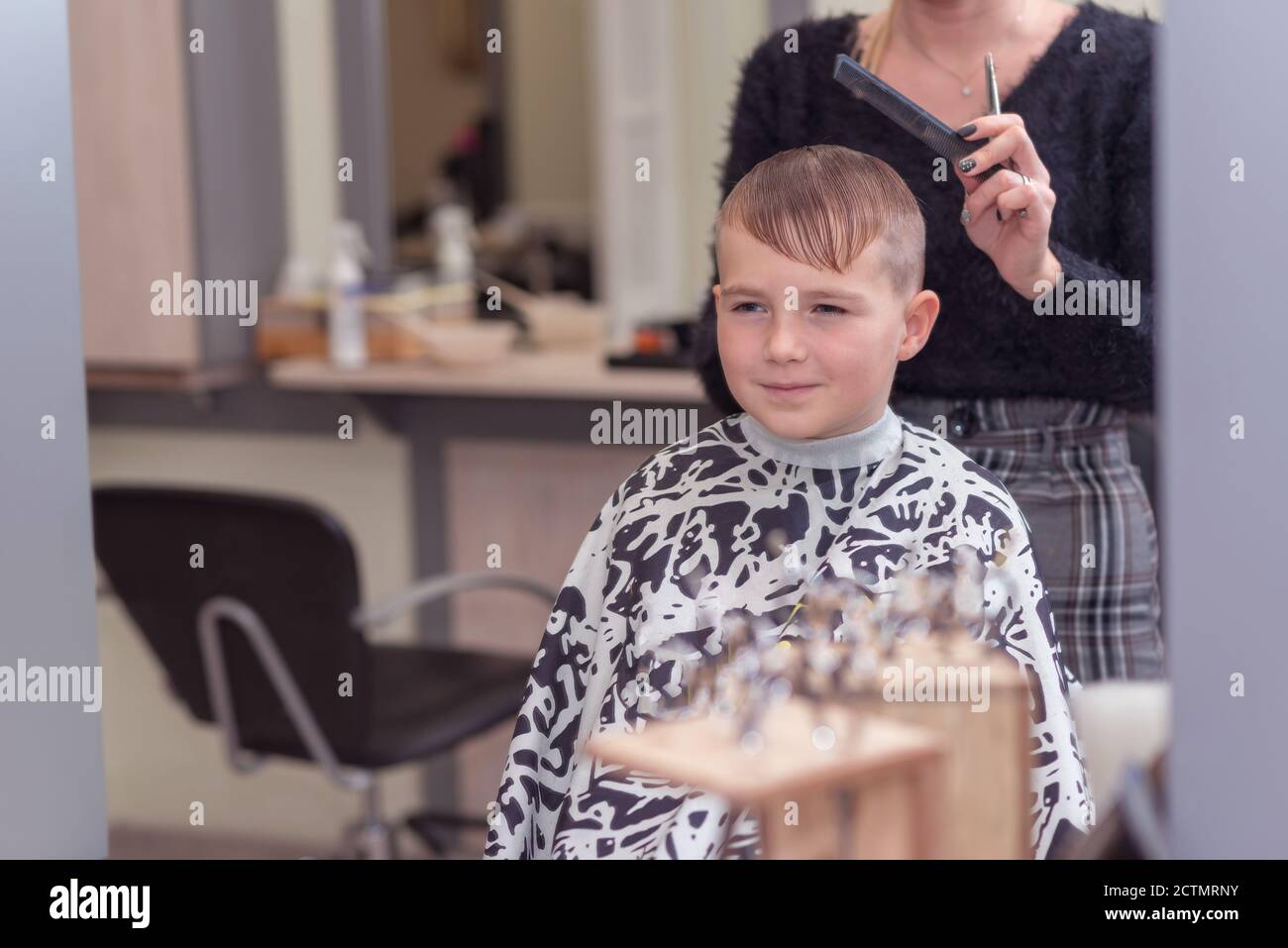 Il ragazzo della scuola giovane sta ottenendo l'acconciatura dal parrucchiere al barbershop.image attraverso lo specchio. Foto Stock