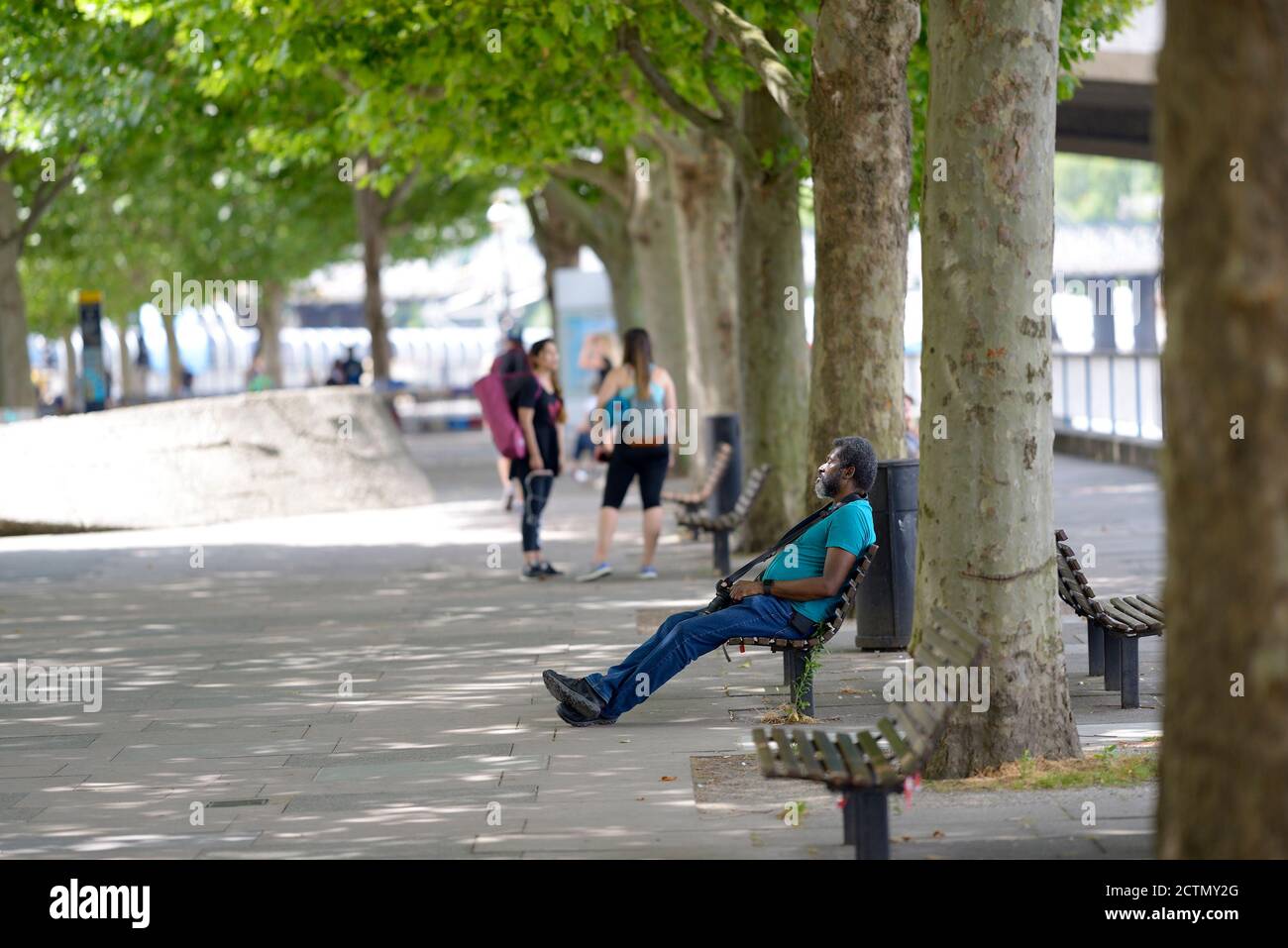 Londra, Inghilterra, Regno Unito. Fotografo che si rilassa su una panchina sulla sponda sud, in una giornata di sole a luglio Foto Stock