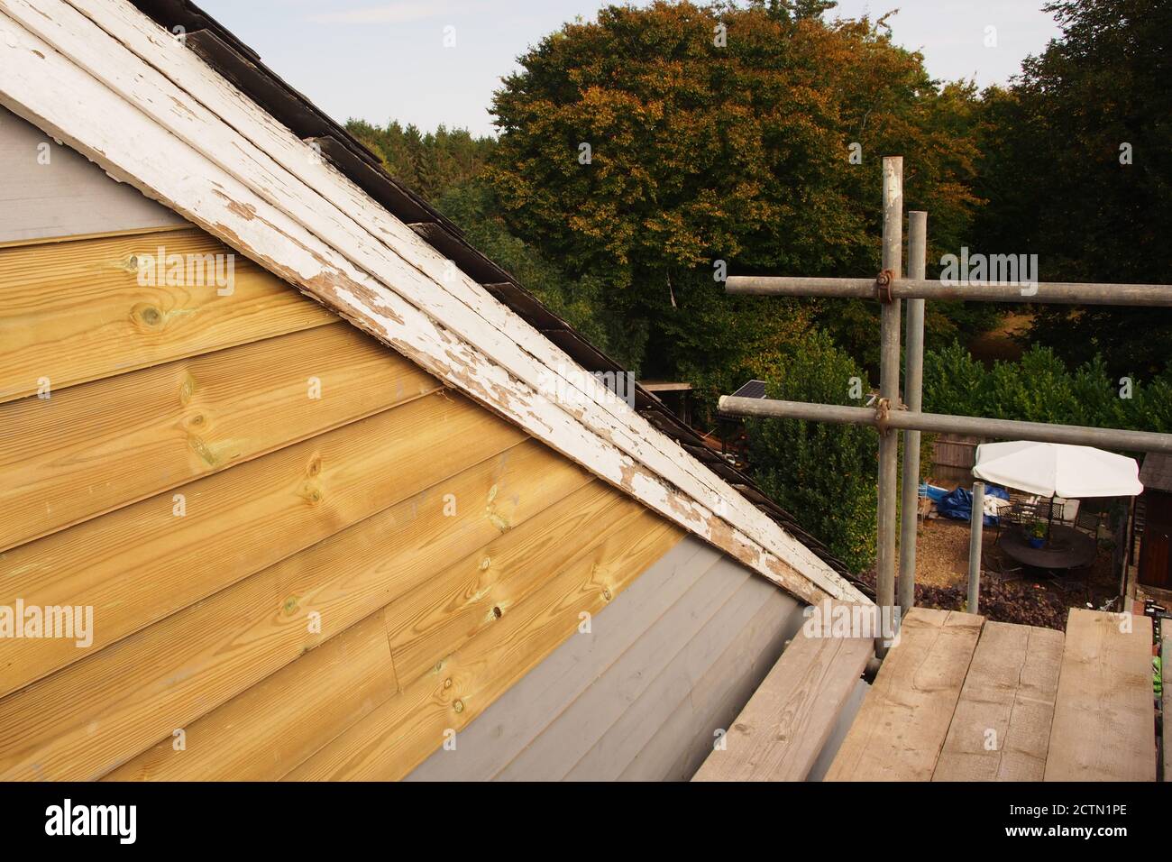 Una vista dall'impalcatura dell'estremità riparata del manto di una vecchia casa rivestita di legno, con tetto di ardesia, ancora da verniciare, più vecchie tavole di chiatta Foto Stock