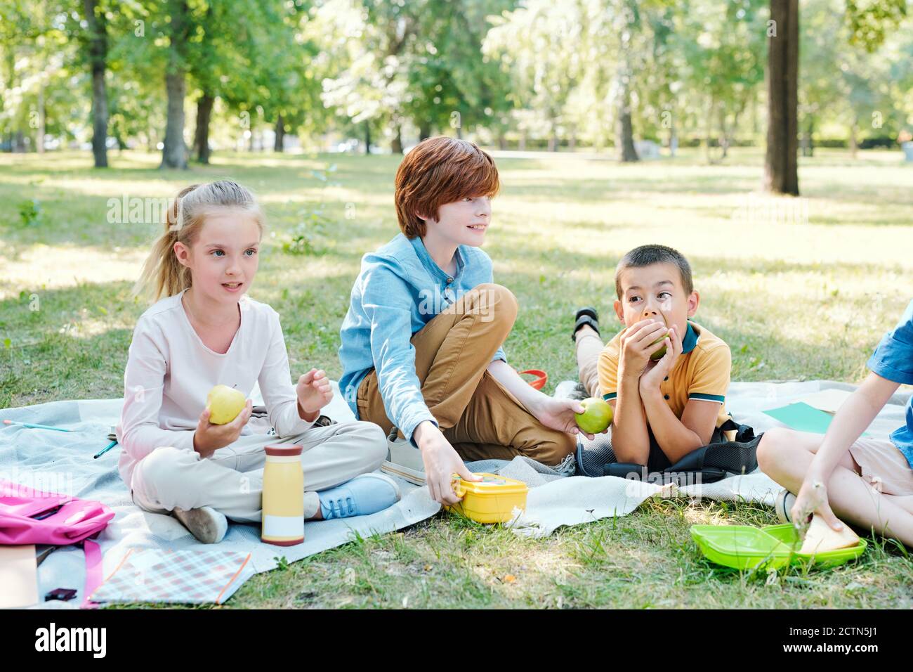 Gruppo di bambini seduti su coperte e pranzo mentre fare un picnic nel parco dopo la scuola Foto Stock