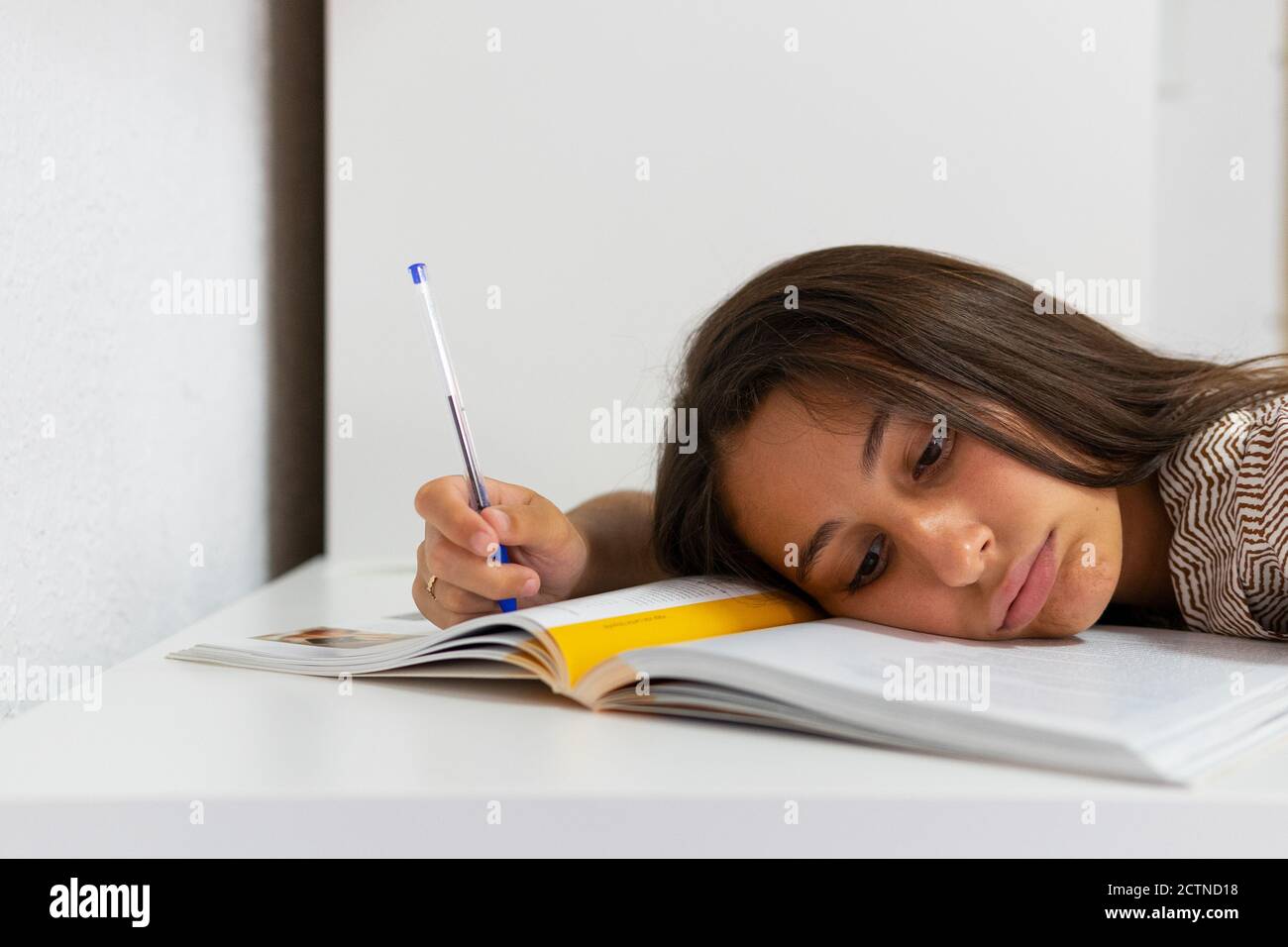 Studentessa esausta sdraiata sul tavolo con libro di testo e penna e dormire durante la preparazione all'esame Foto Stock