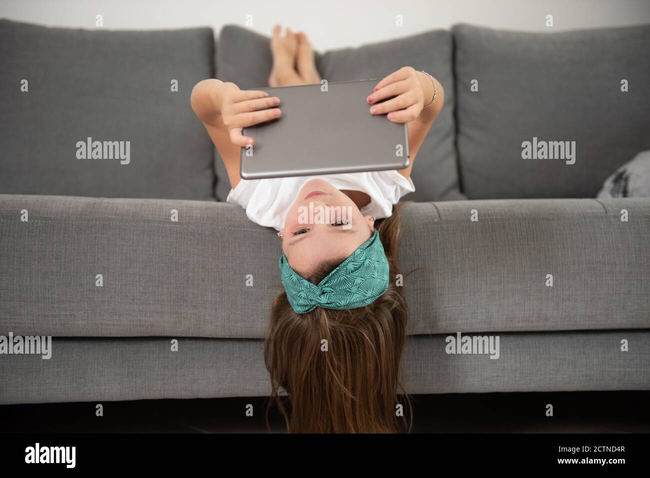 Bambina sdraiata sul divano mentre era intrattenuta utilizzo del tablet durante il fine settimana Foto Stock