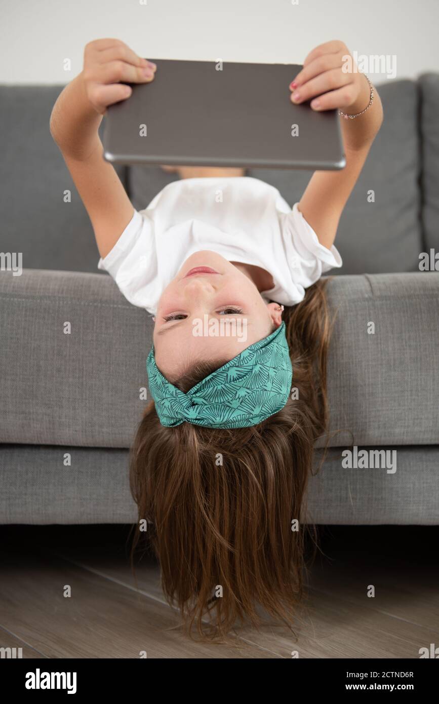 Bambina sdraiata sul divano mentre era intrattenuta utilizzo del tablet durante il fine settimana Foto Stock