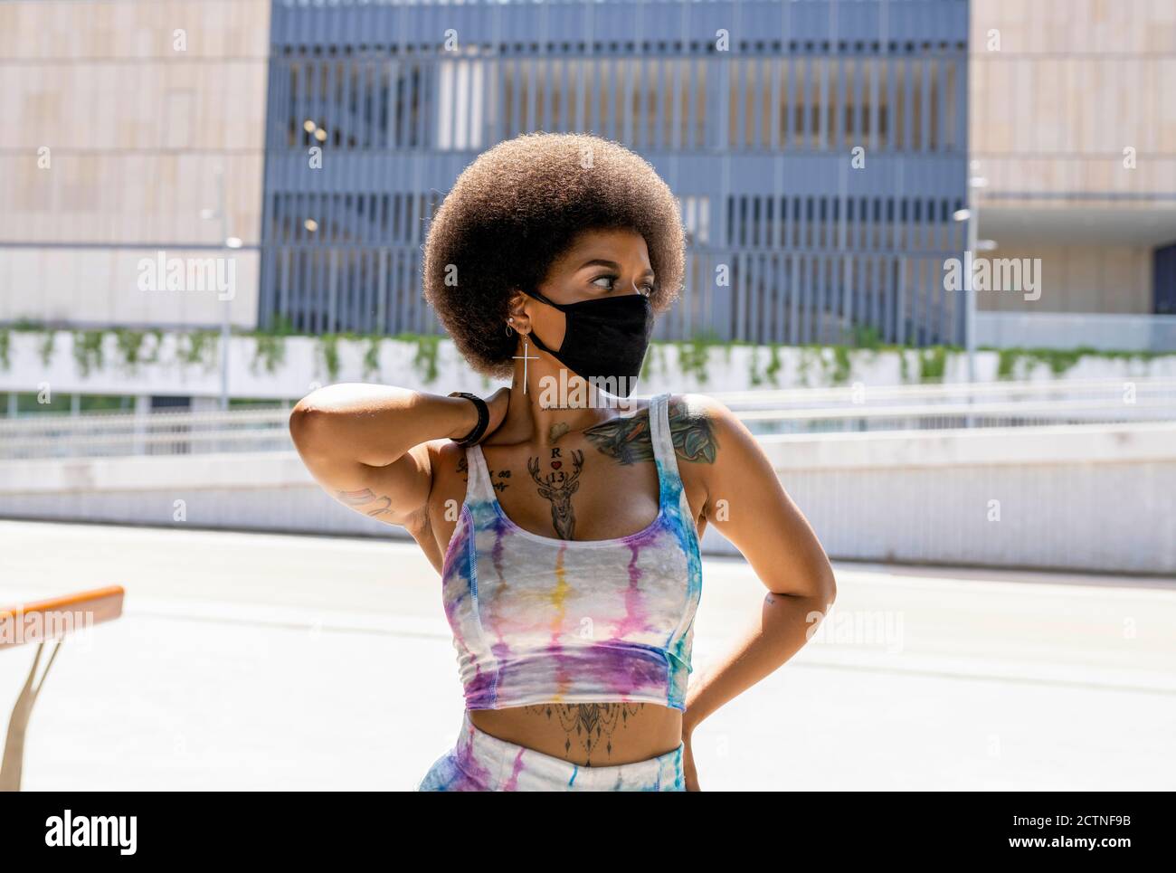 Donna afro-americana sicura in maschera medica e estate alla moda outfit in piedi in zona urbana in città durante l'epidemia di coronavirus Foto Stock