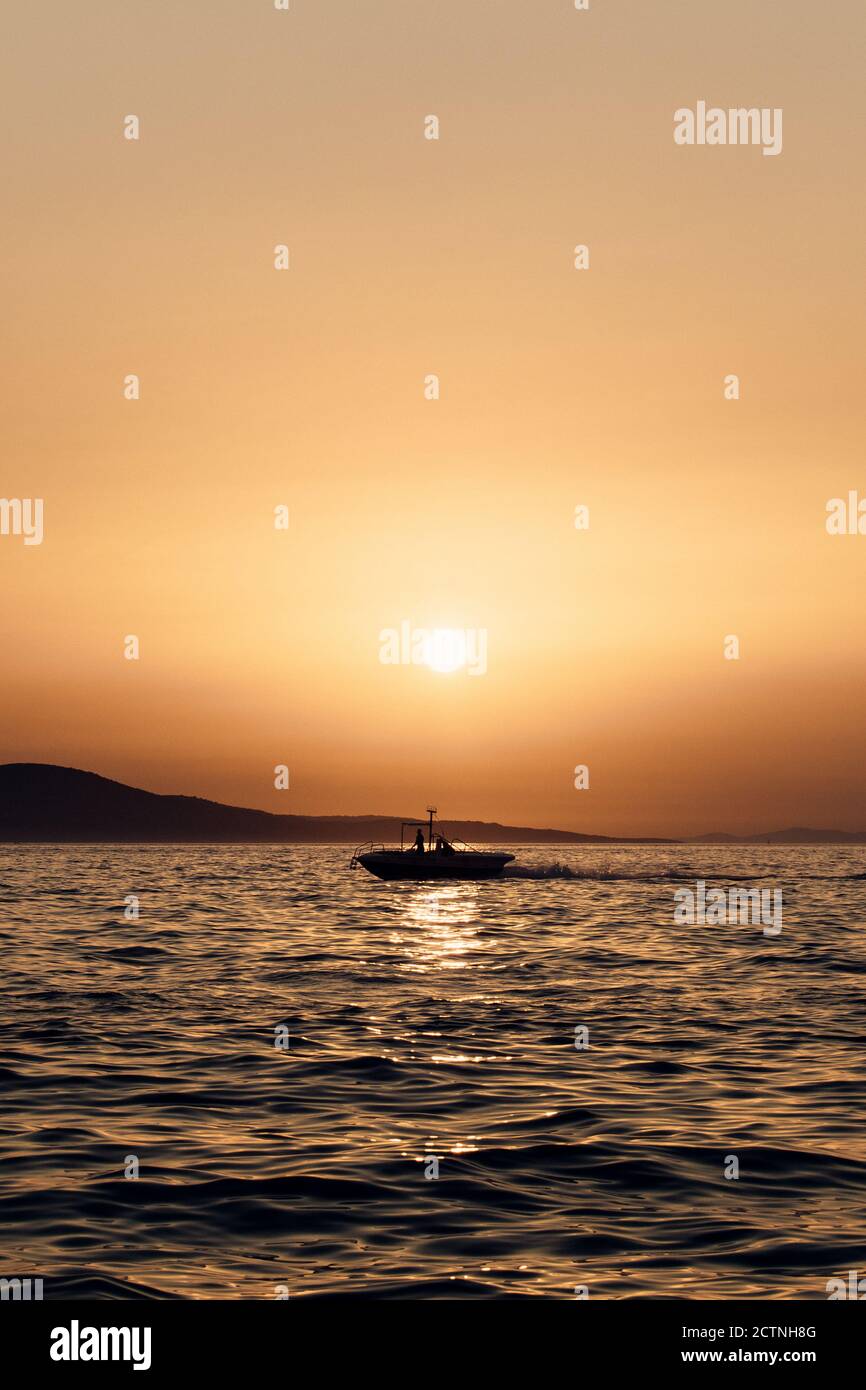 Silhouette di nave marina solitaria che galleggia sulle acque di mare ondulate Contro il cielo arancione del tramonto in Croazia Foto Stock