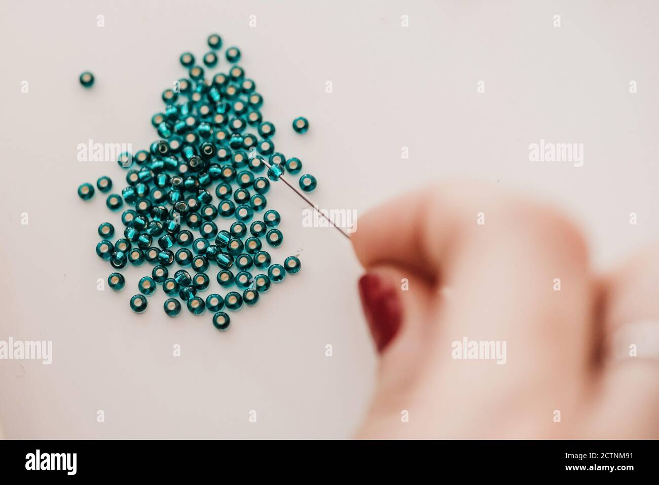 Da sopra closeup di perline artiche femminili irriconoscibili su ago durante il lavoro in officina Foto Stock