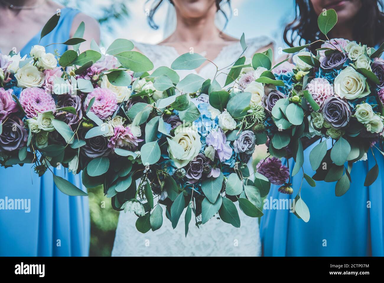 Una sposa e le sue bridesmaid che tengono il loro bouquet in su per una foto con un blu pastello, bianco e verde tema ai fiori. Foto Stock