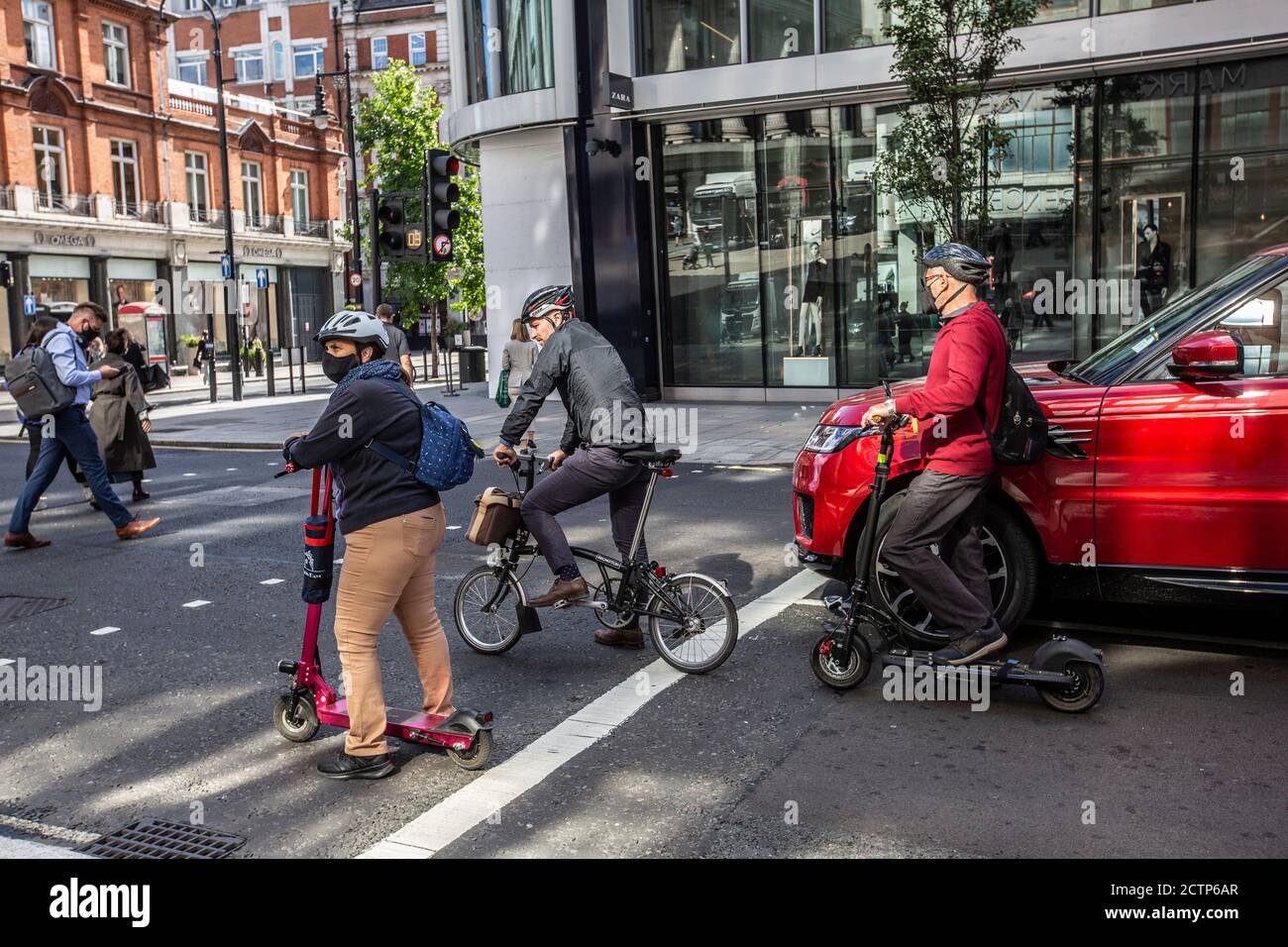 I piloti di Electric Scooter si schierano contro un ciclista su Oxford Street a un semaforo tra il traffico diurno, Londra, Inghilterra, Regno Unito Foto Stock