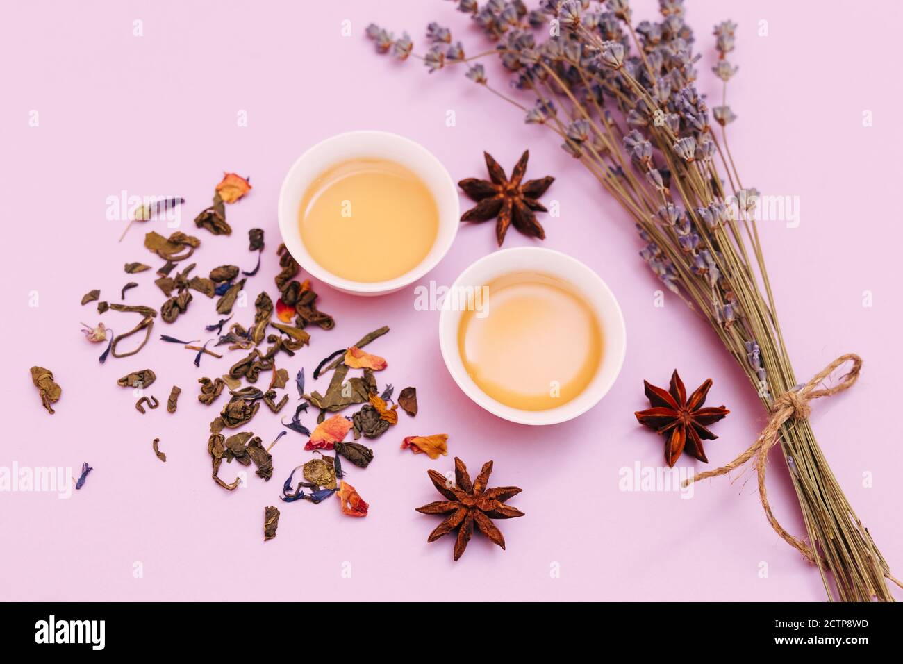 Due tazze piene di tè primaverile fresco e foglie di tè essiccato sparse, isolate su uno sfondo pulito. Foto Stock