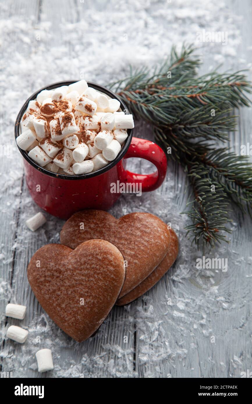 Tazza di cacao caldo con marshmallow e pan di zenzero di Natale sotto forma di cuore su uno sfondo di legno nevoso. Cartolina di Natale. Foto Stock