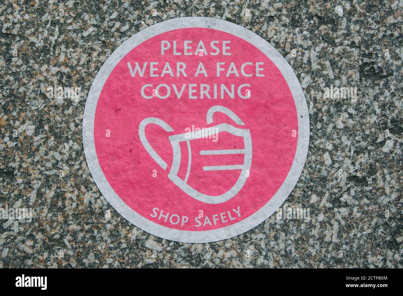Primo piano di un segno in un negozio con un Maschera immagine e testo si prega di indossare una copertura facciale Foto Stock