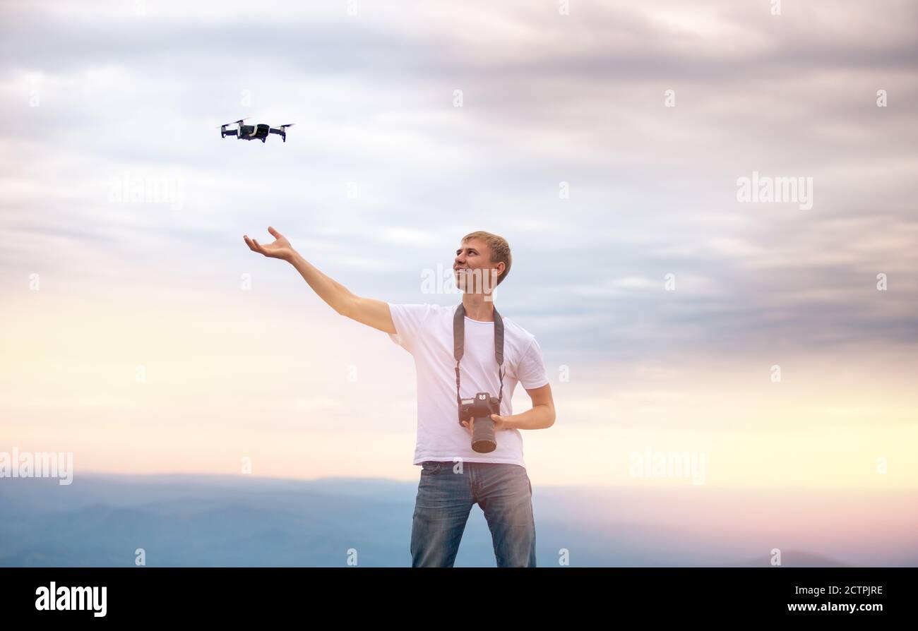 Happy man fotografo con fotocamera controlli drone, effettua quadcopter atterraggio a portata di mano, tramonto Foto Stock