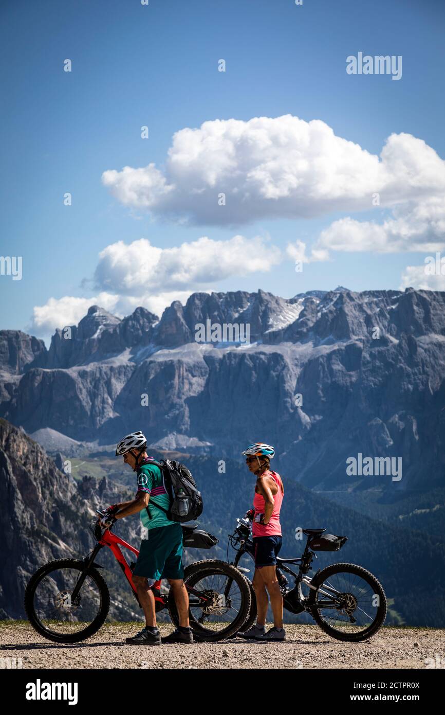 Due ciclisti con mountain bike ammirano la vista del Massiccio del Sella fuori dalla stazione della funivia Seceda , Val Gardena, Italia. Foto Stock