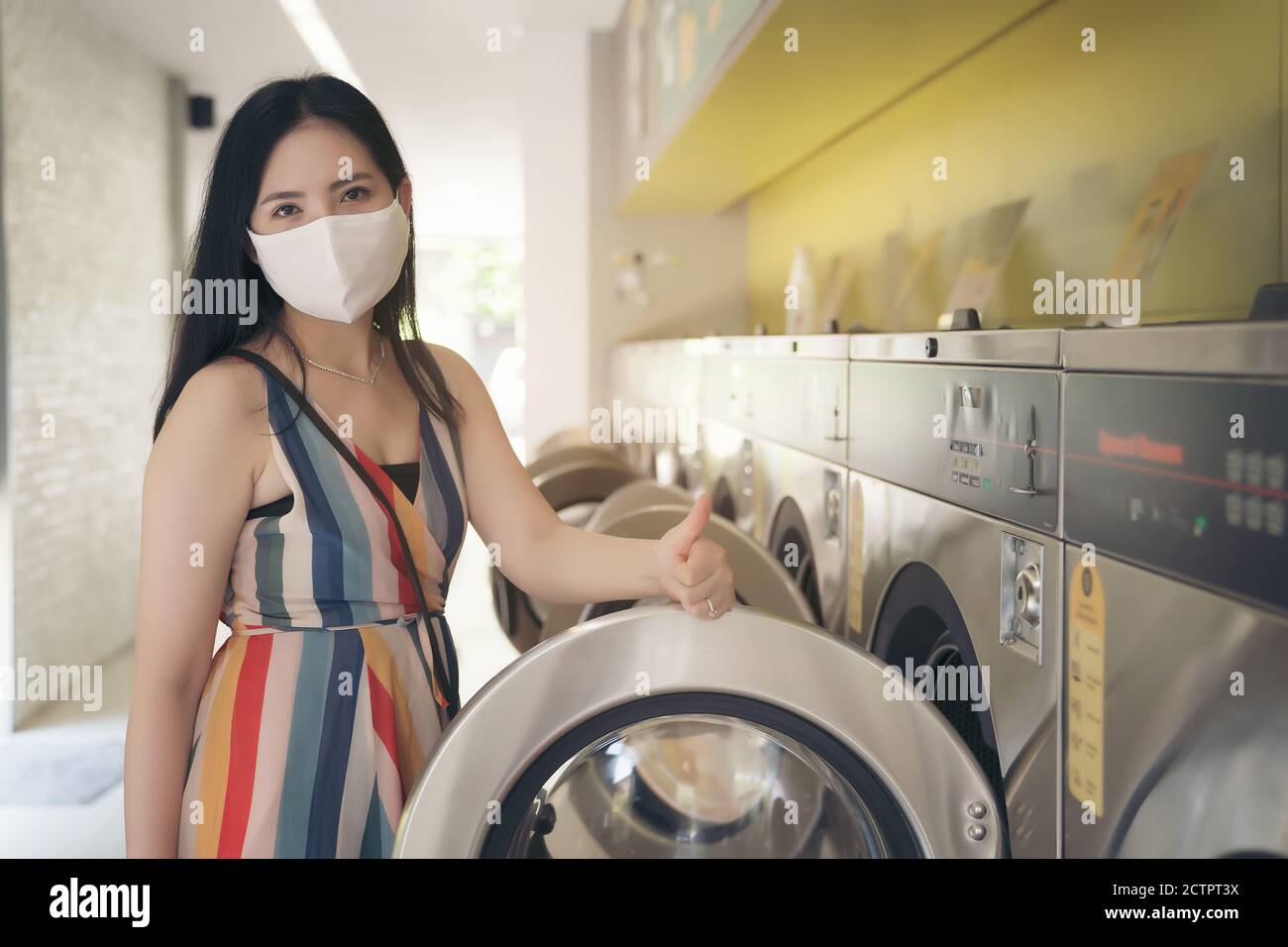 Bella donna con maschera facendo lavanderia al negozio di lavanderia automatica. Foto Stock