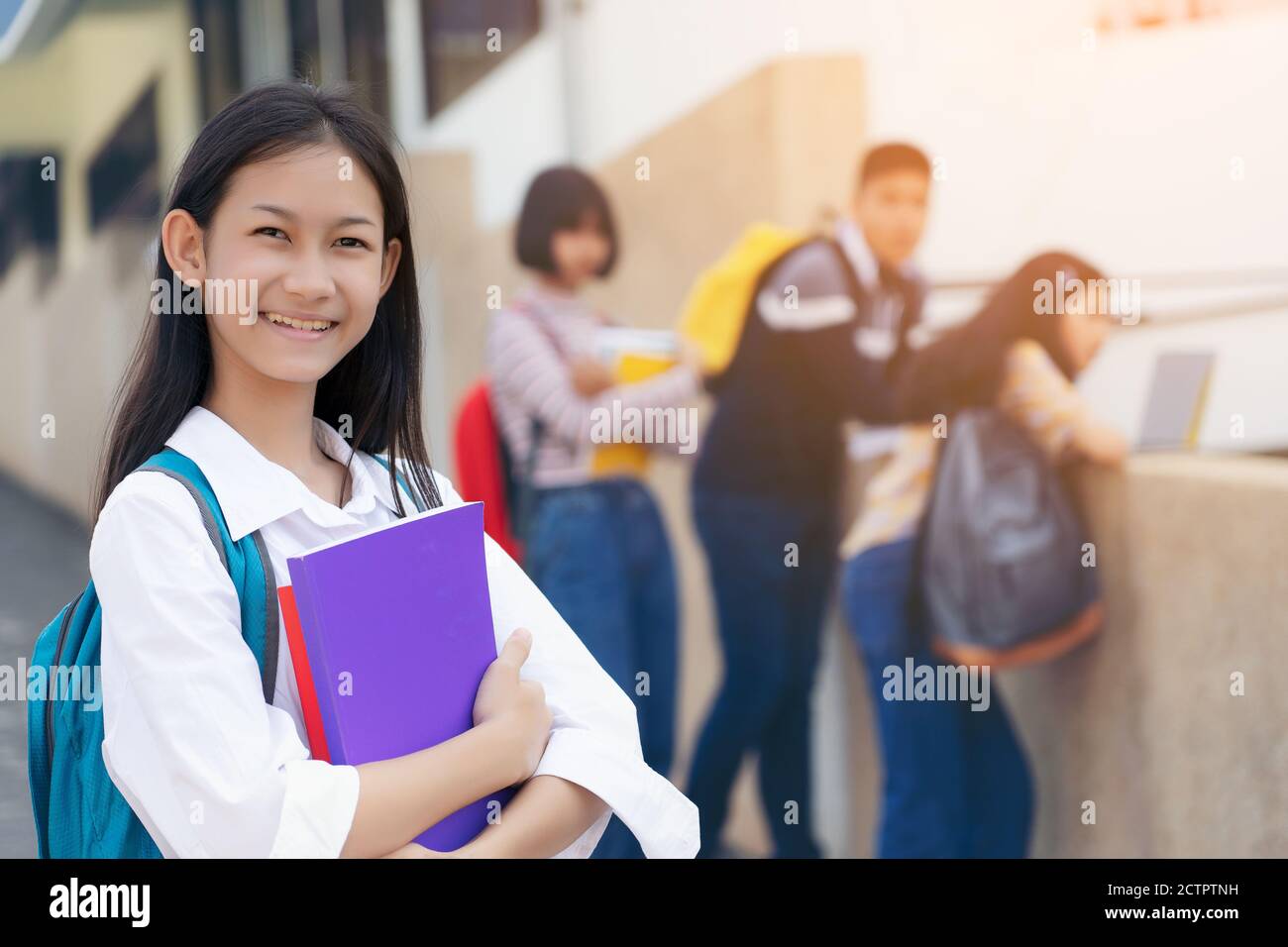 giovane studente adolescente ragazza studente di scuola superiore che porta borsa di studio holding notebook con amici in background Foto Stock